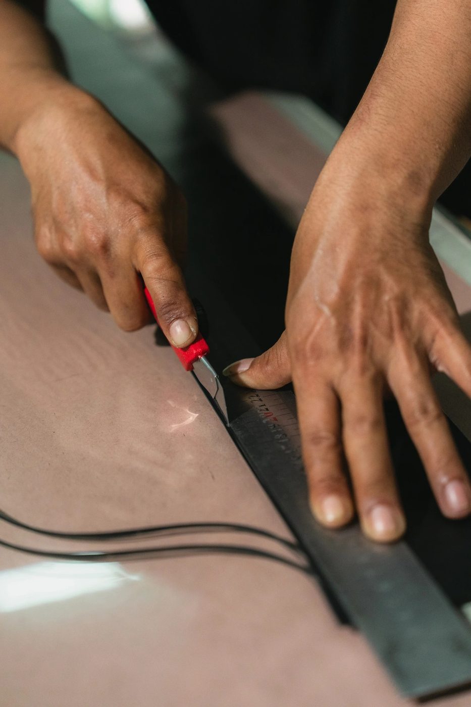 Artisan cutting a black leather strap with a utility knife and steel ruler
