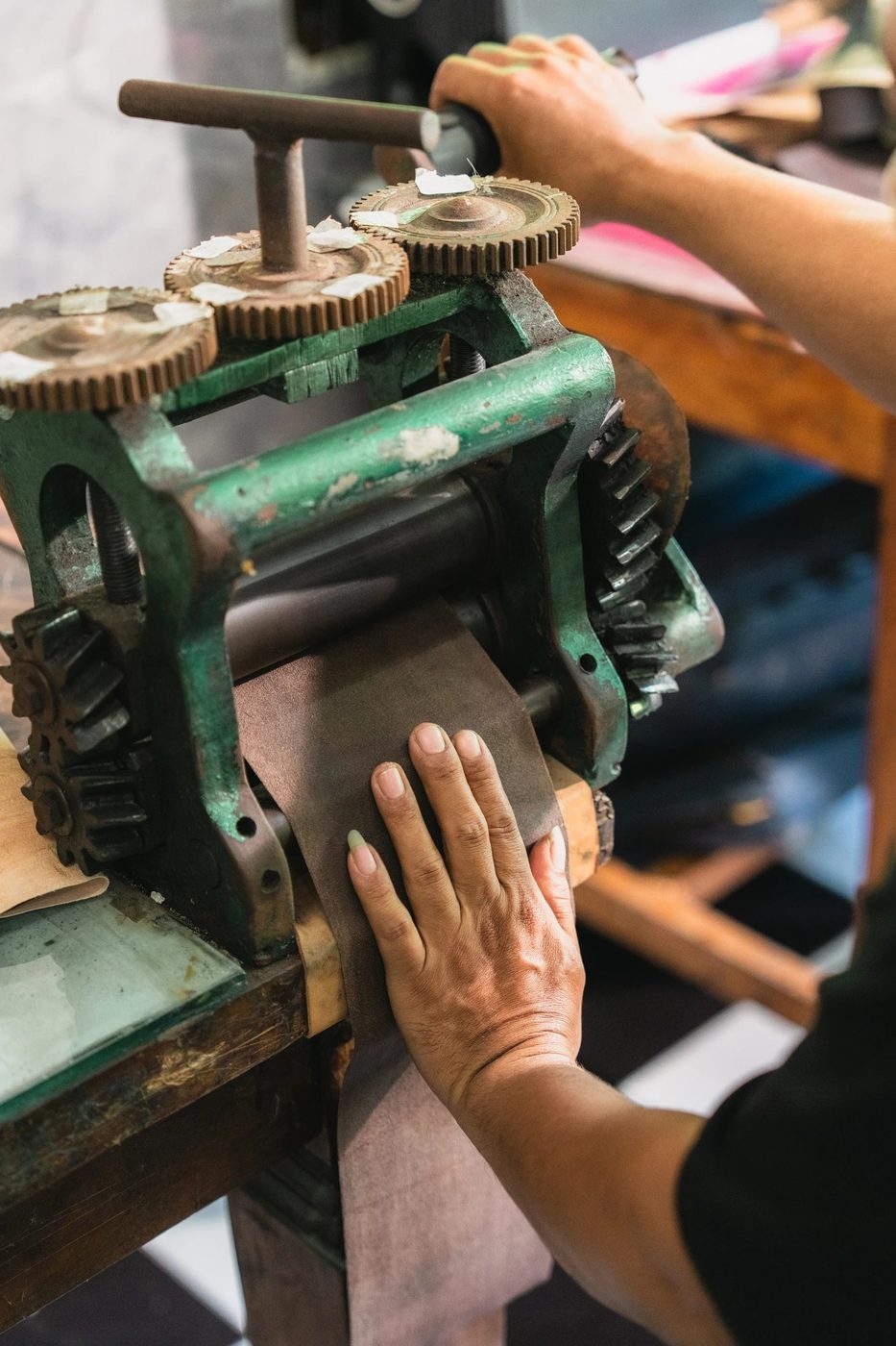 Artisan feeding brown leather through a hand-crank leather splitting machine