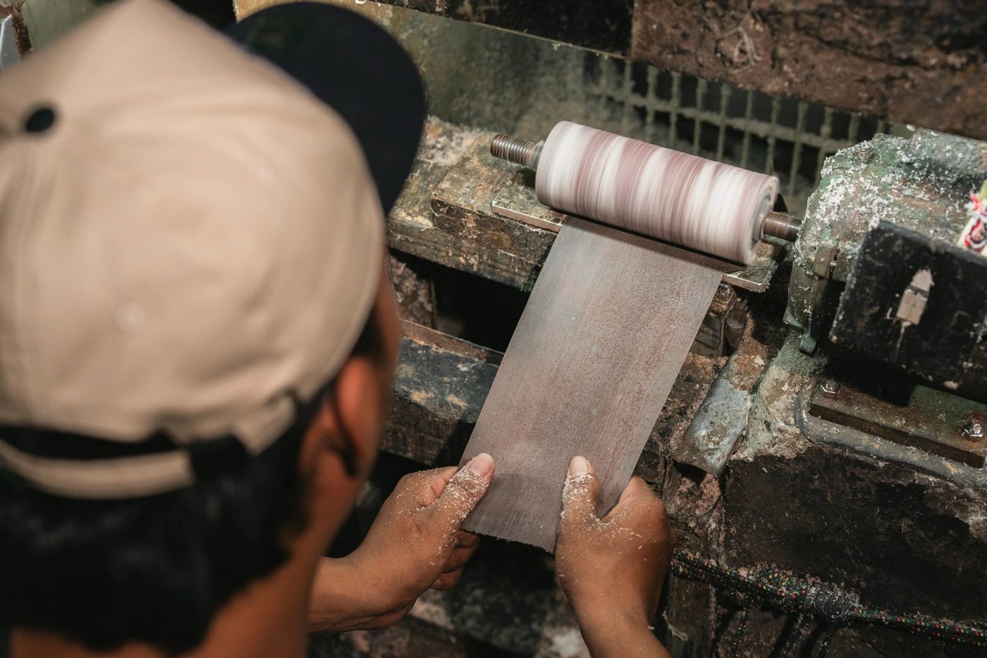 Artisan in a cap guiding a leather panel through a workshop roller machine