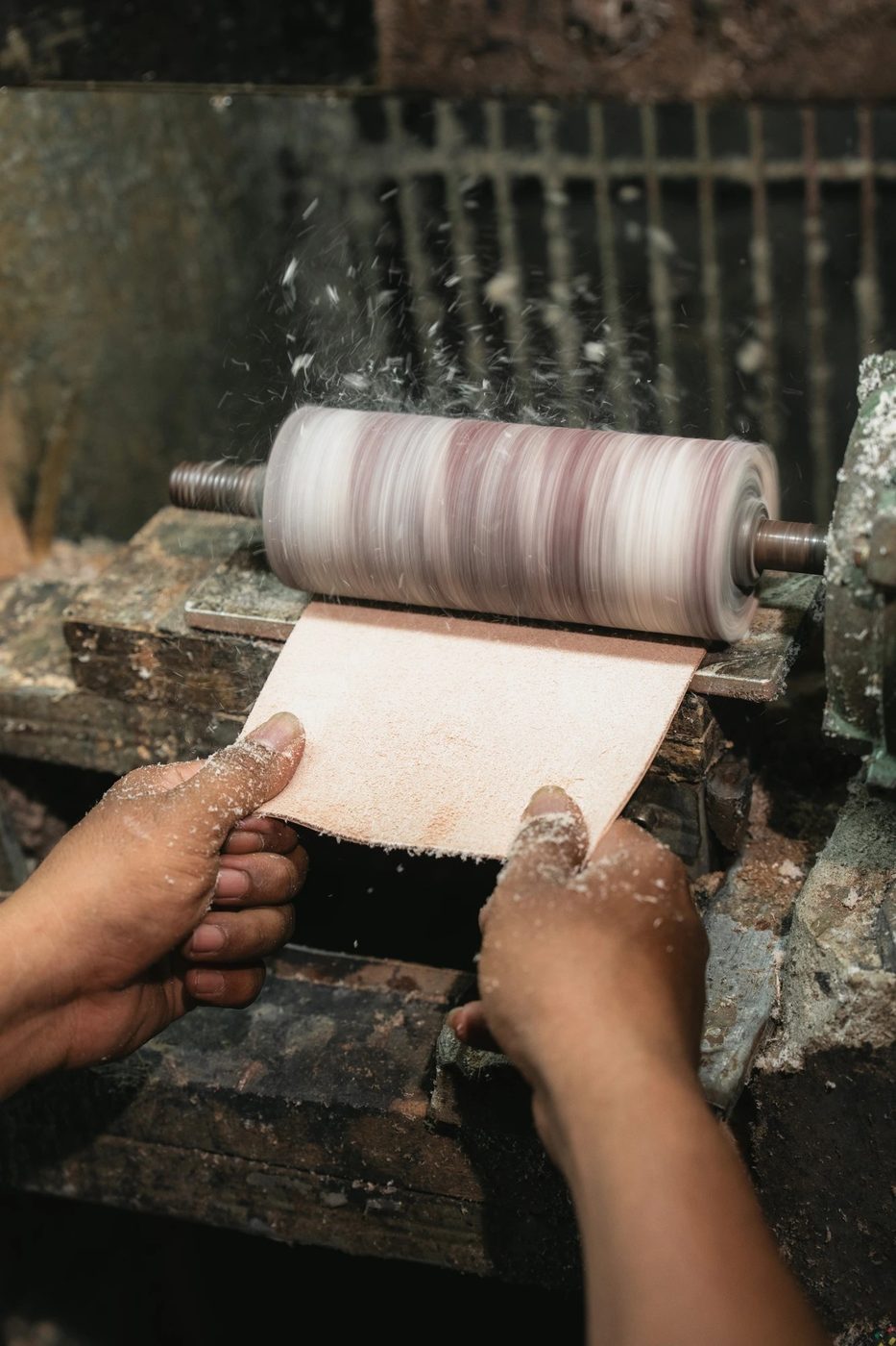 Hands shaping a leather panel against a spinning roller, dust in the air