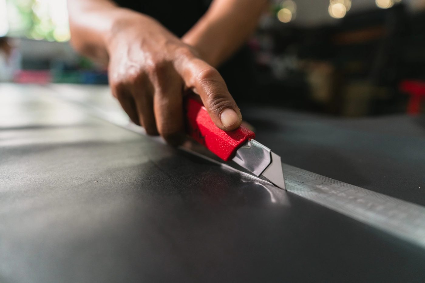 Cutting a grey leather strap with a red utility knife along a steel ruler